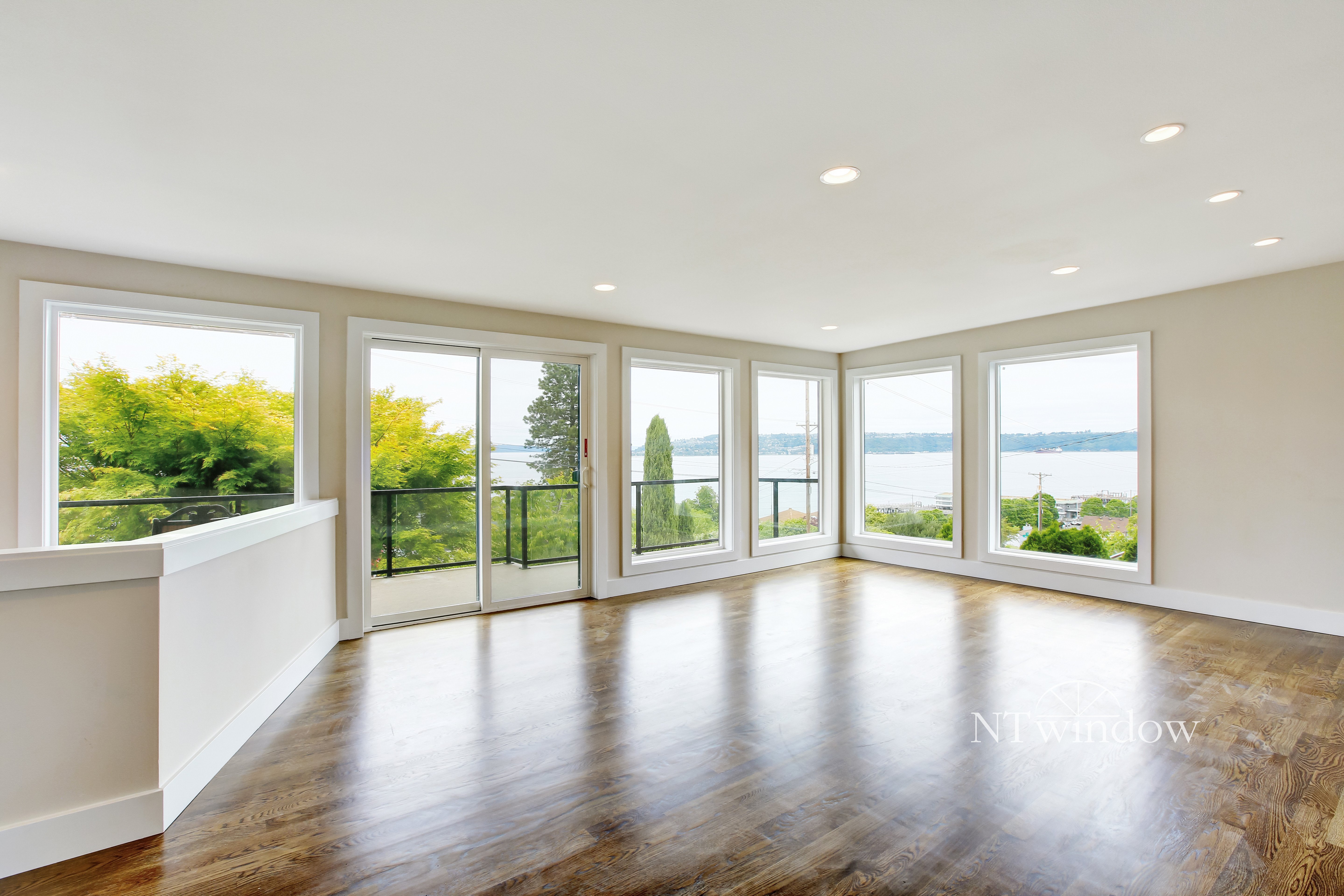 Spacious living room with large windows overlooking a scenic view of trees and water, featuring wooden flooring.