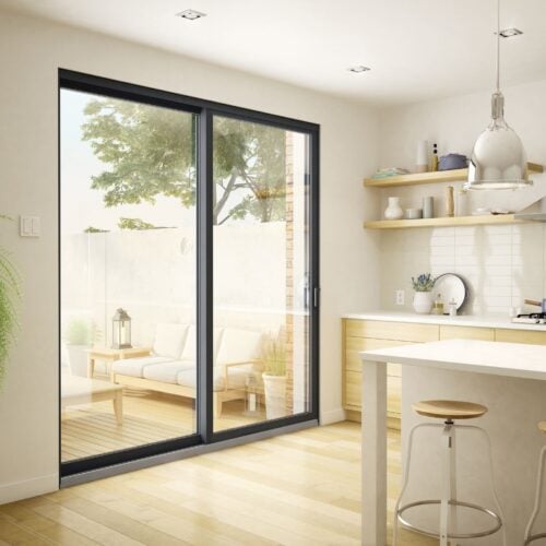 A modern kitchen with a large glass door leading to an outdoor seating area, wooden shelves, and light wood flooring.